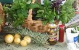 A basket of bunches of basil on a table with few fruit, sprigs of rosemary, and bottled goods in front of the basket.