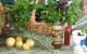 A basket of bunches of basil on a table with few fruit, sprigs of rosemary, and bottled goods in front of the basket.