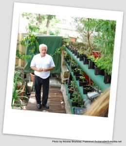 Man in white t-shirt standing next to his vertical rows of potted food plants