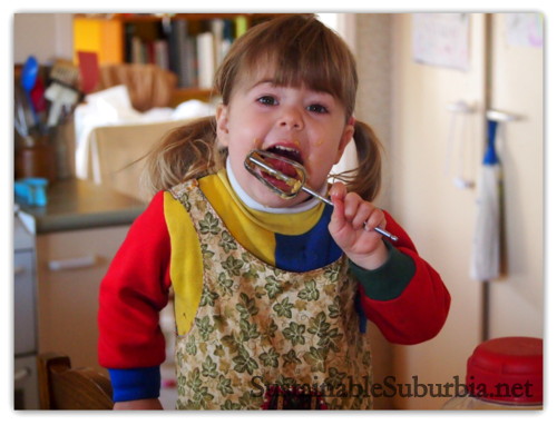 A three year old in the kitchen, licking the mixer